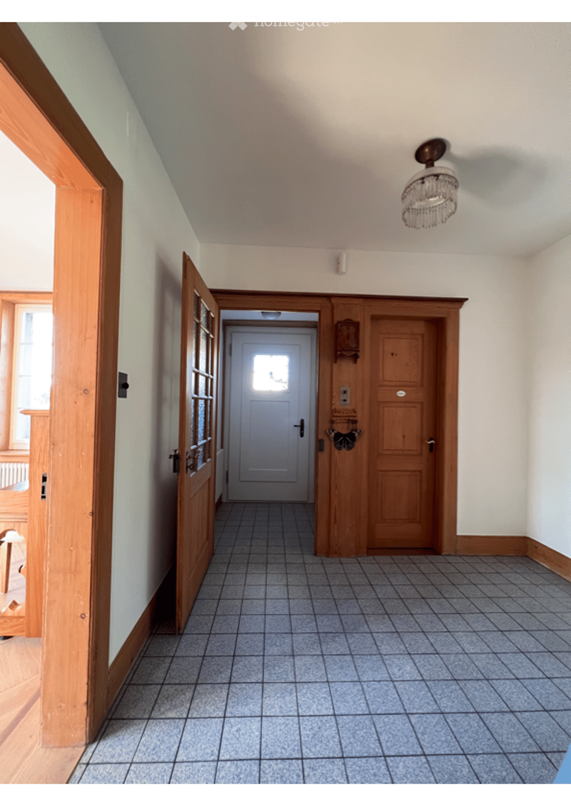 Empty hallway with tiled floor, wooden doors, and a chandelier light fixture.