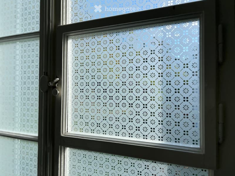 Close-up of a window with decorative, patterned glass featuring floral and geometric designs in shades of blue, green, and black.