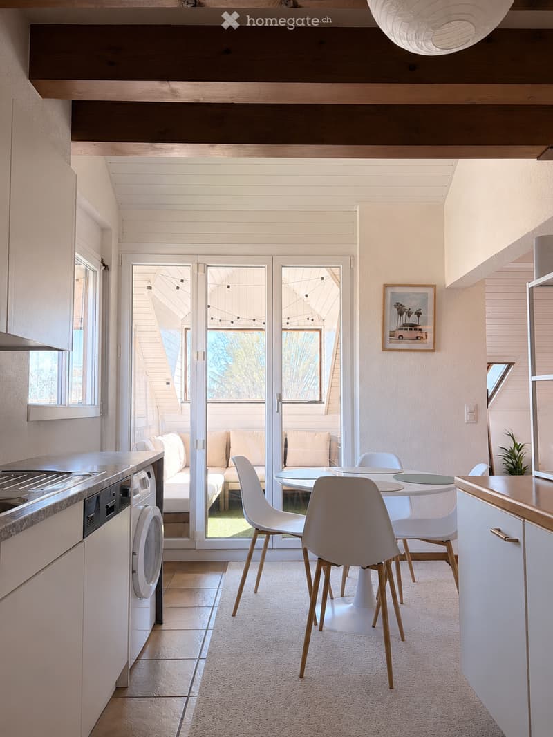 Furnished Room. Open-plan living and dining area with a sofa, dining table, chairs, and a kitchen counter with a dishwasher. Large windows and sliding doors lead to an outdoor space.