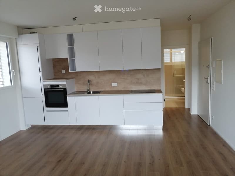 Modern kitchen with white cabinets, stainless steel oven, sink, and faucet, adjacent to a bathroom with a glass shower enclosure.