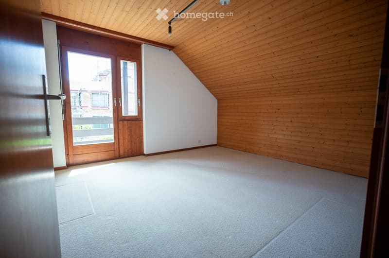 Empty room with wooden walls, carpeted floor, and large wooden door leading to a balcony.