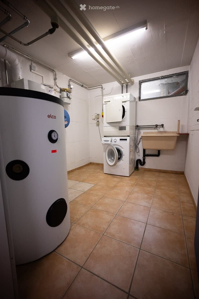 Utility room with a washing machine, water heater, and sink, featuring tiled flooring and exposed pipes.