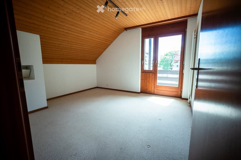 Empty room with wooden ceiling, carpeted floor, and large wooden door leading to a balcony.