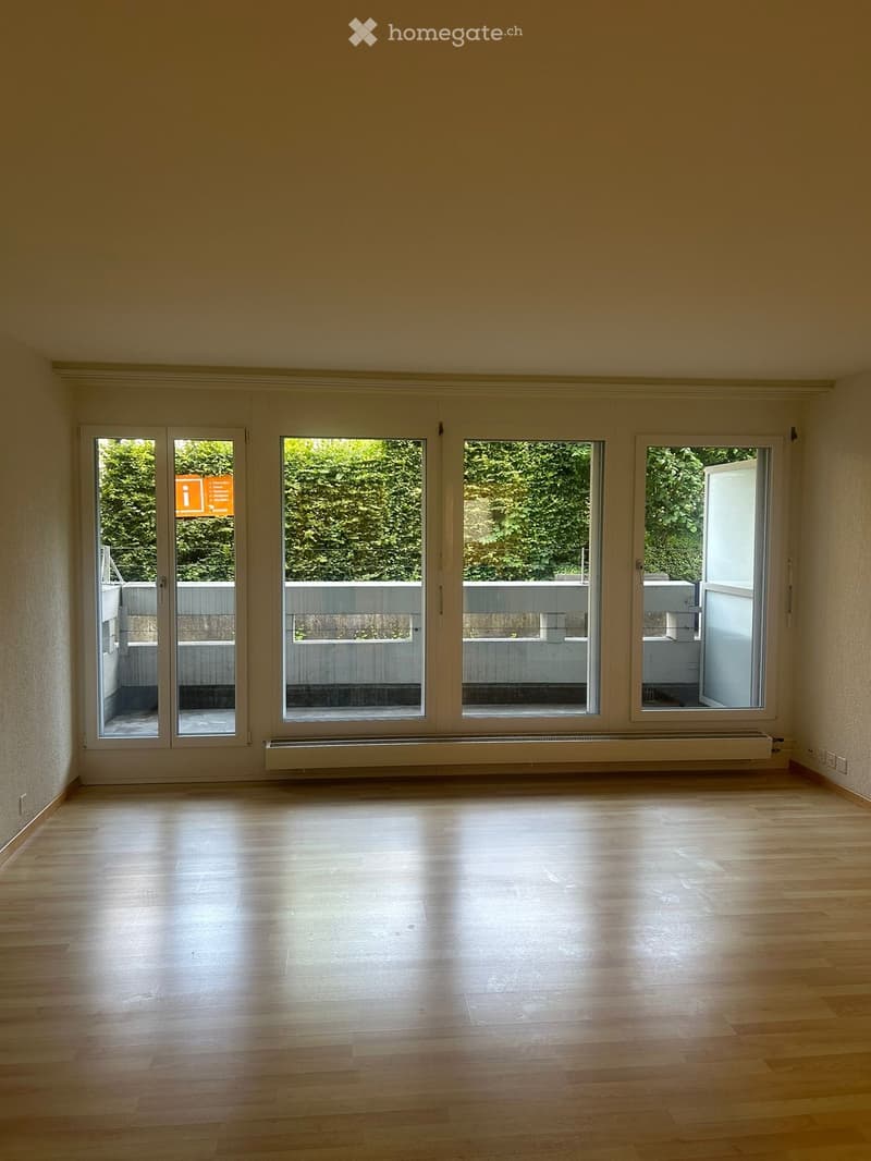 Empty room with wooden flooring, large windows, and a radiator. No furniture or equipment present.