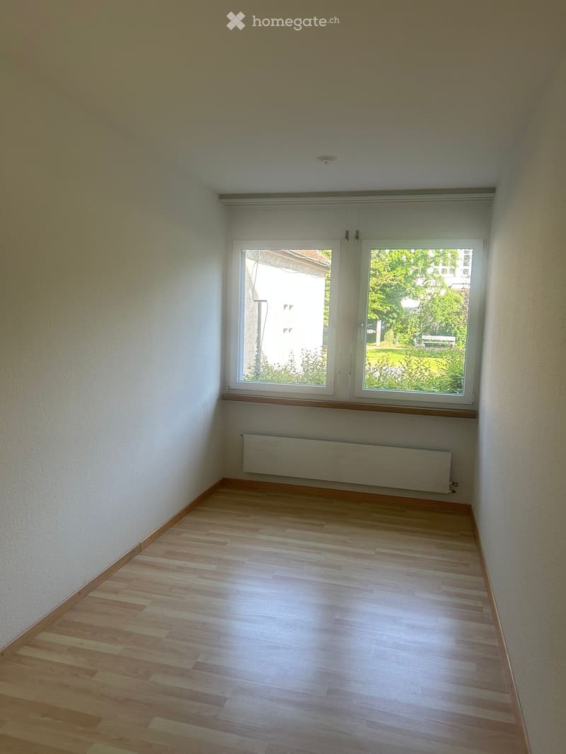 Empty room with wooden flooring, white walls, and a large window with a radiator below it.