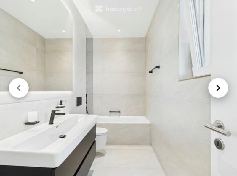 Modern bathroom with a double sink, sleek faucet, bathtub, toilet, and a large mirror. The space features clean lines, neutral tones, and contemporary fixtures.