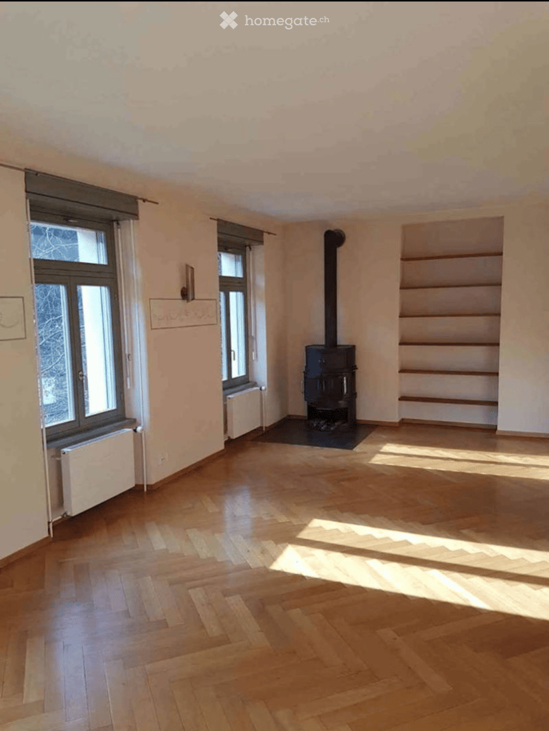 Empty room with wooden flooring, large windows, and a fireplace. No furniture or equipment present.
