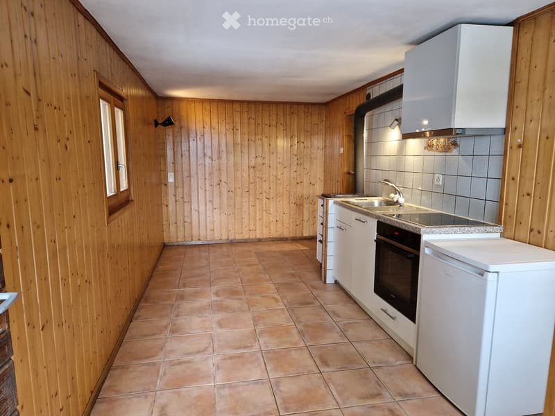 Modern kitchen with wooden walls, tiled floor, white cabinets, sink, oven, and refrigerator.