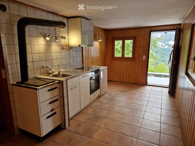 Modern kitchen with white cabinets, stainless steel appliances, tiled floor, and a scenic mountain view through the open door.