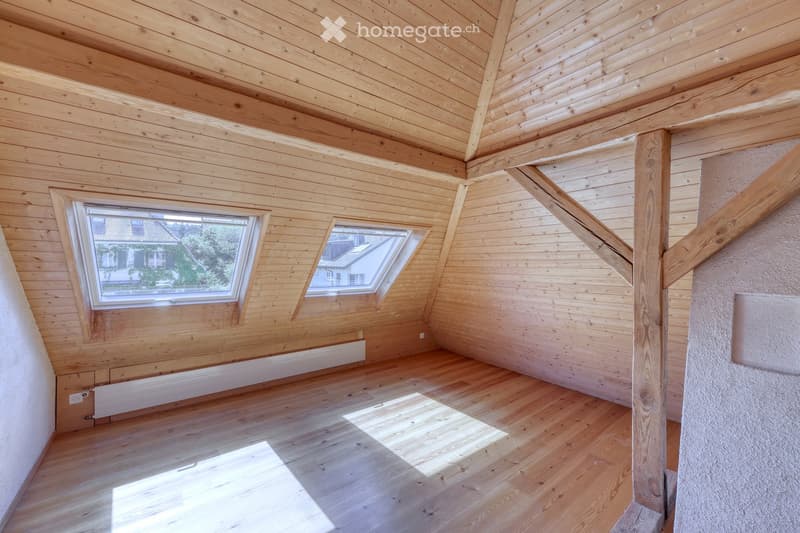 Empty attic room with wooden walls, ceiling, and floor, featuring two skylight windows and exposed wooden beams.