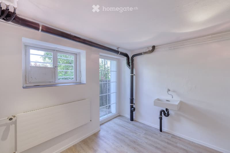 Empty room with white walls, wooden flooring, a radiator, a window, and a sink with visible plumbing.