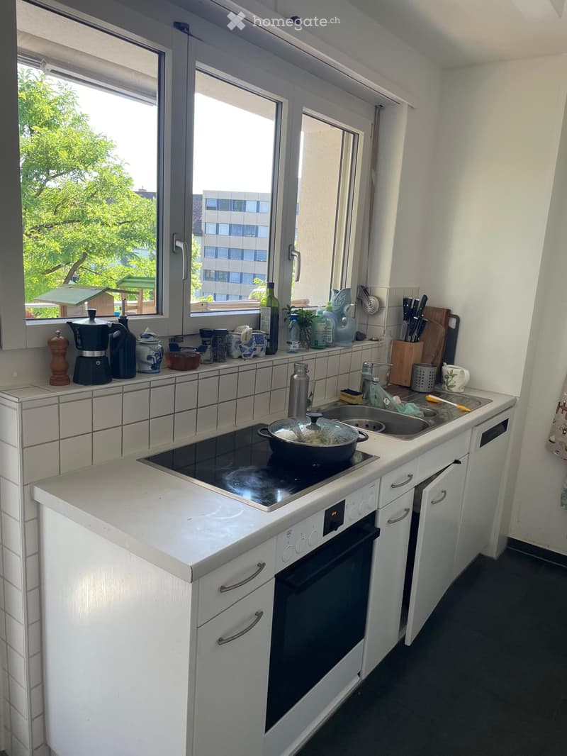 Modern kitchen with white cabinets, black countertop, built-in oven, sink, and various appliances and utensils on the counter.