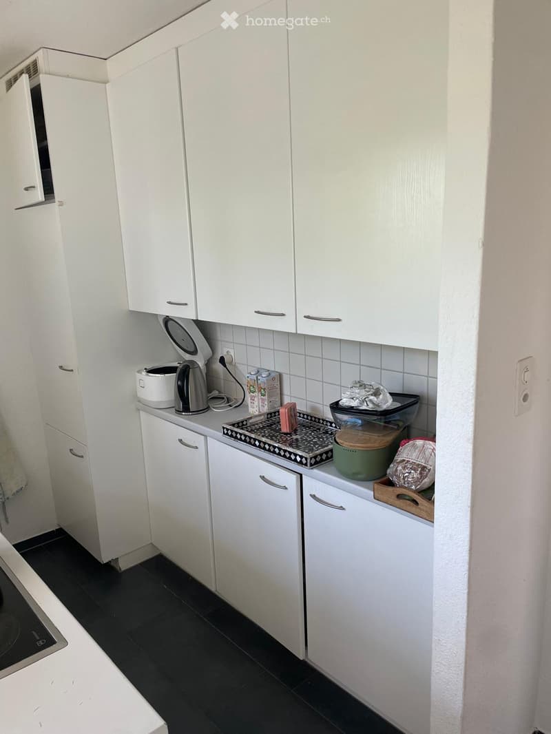 A modern kitchen with white cabinets, a black tiled floor, and various appliances including an oven, microwave, kettle, and a tray with items on the counter.