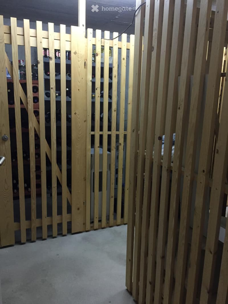 A narrow hallway with a wooden gate on one side and shelves on the other, featuring a carpeted floor and exposed wooden beams on the ceiling.