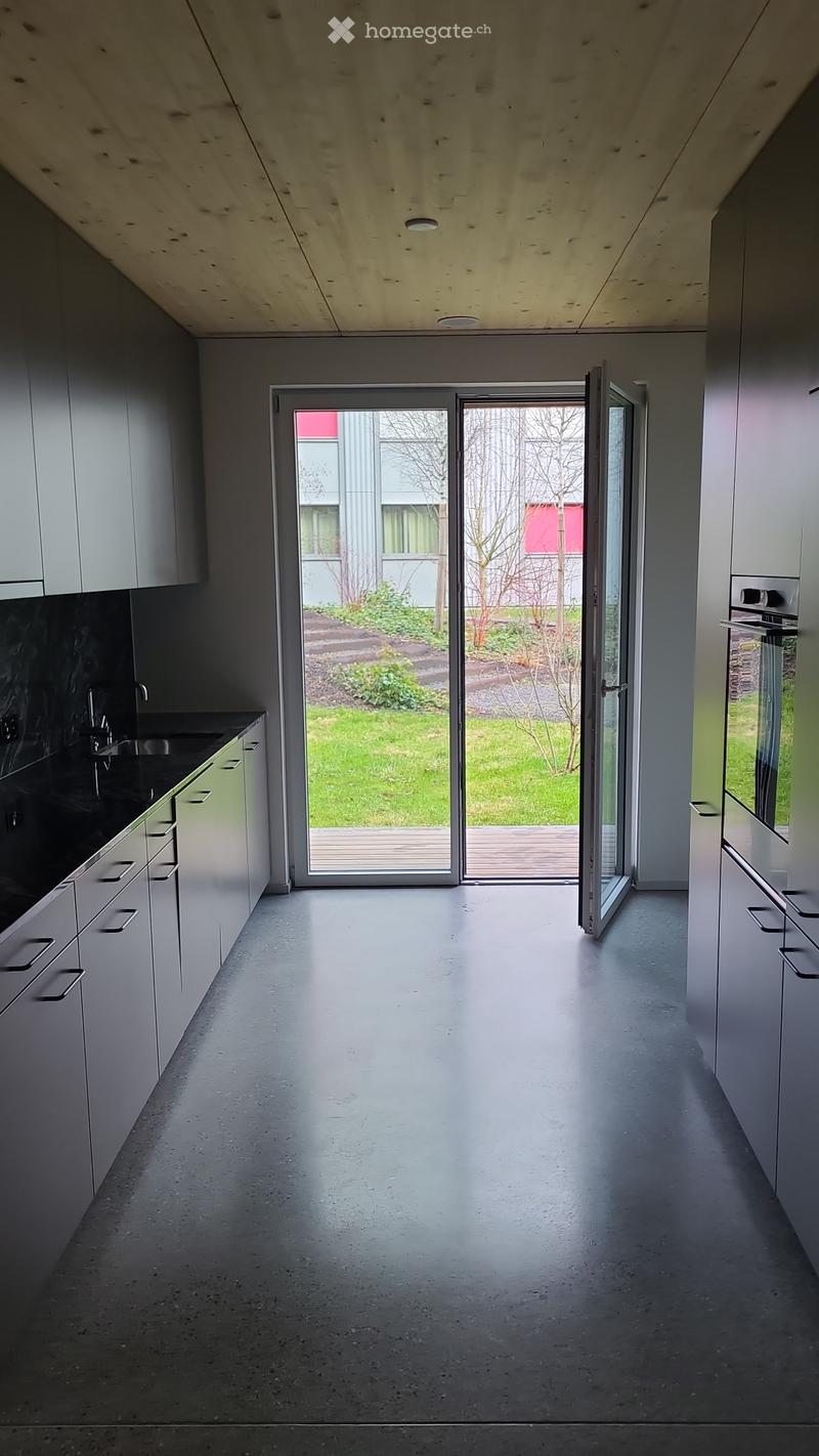 Modern, minimalist hallway with grey cabinets, a large sliding glass door leading to a garden, and a polished concrete floor.