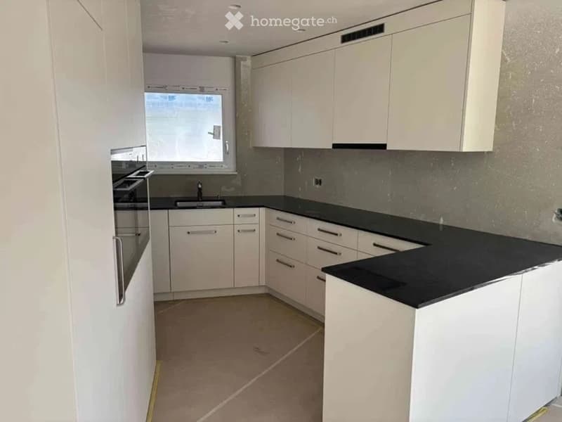 Modern kitchen with white cabinets, black countertops, and stainless steel appliances including a sink and oven.