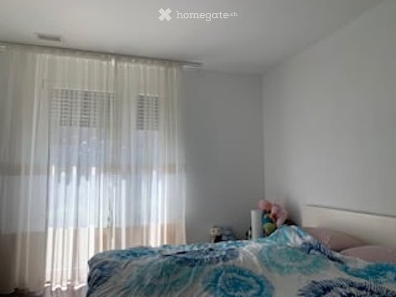 Bedroom with a bed, nightstand, and a curtain. The bed has a blue and white patterned duvet and pink pillows.