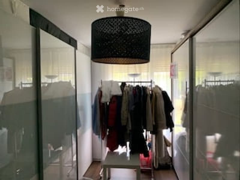 A small, modern walk-in closet with a wardrobe filled with clothes, a large mirror, and a stylish black hanging lamp.