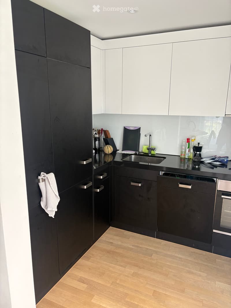 Modern kitchen with black and white cabinets, stainless steel sink, and wooden flooring.