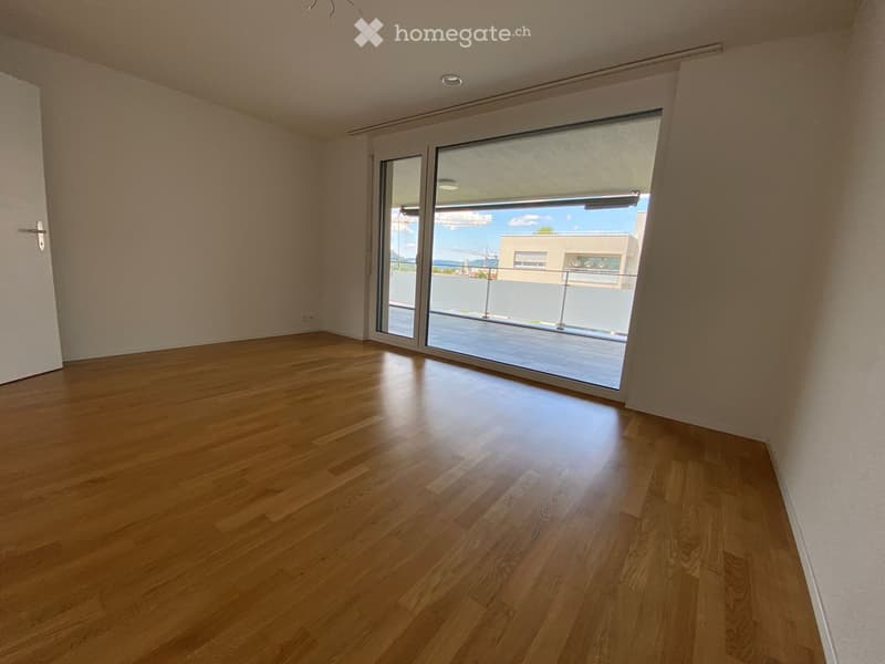 Empty room with wooden flooring, large sliding glass door leading to a balcony, and white walls.