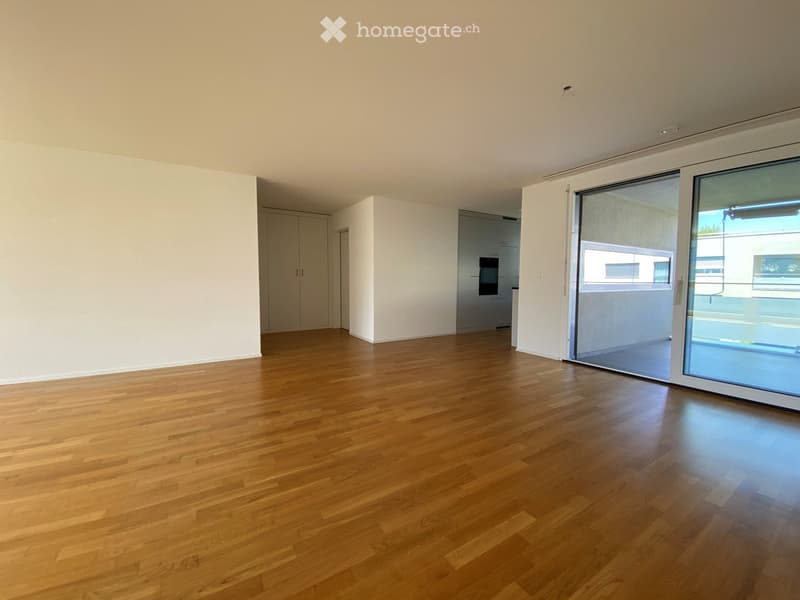 Empty room with wooden flooring, white walls, and large sliding glass doors leading to a balcony.