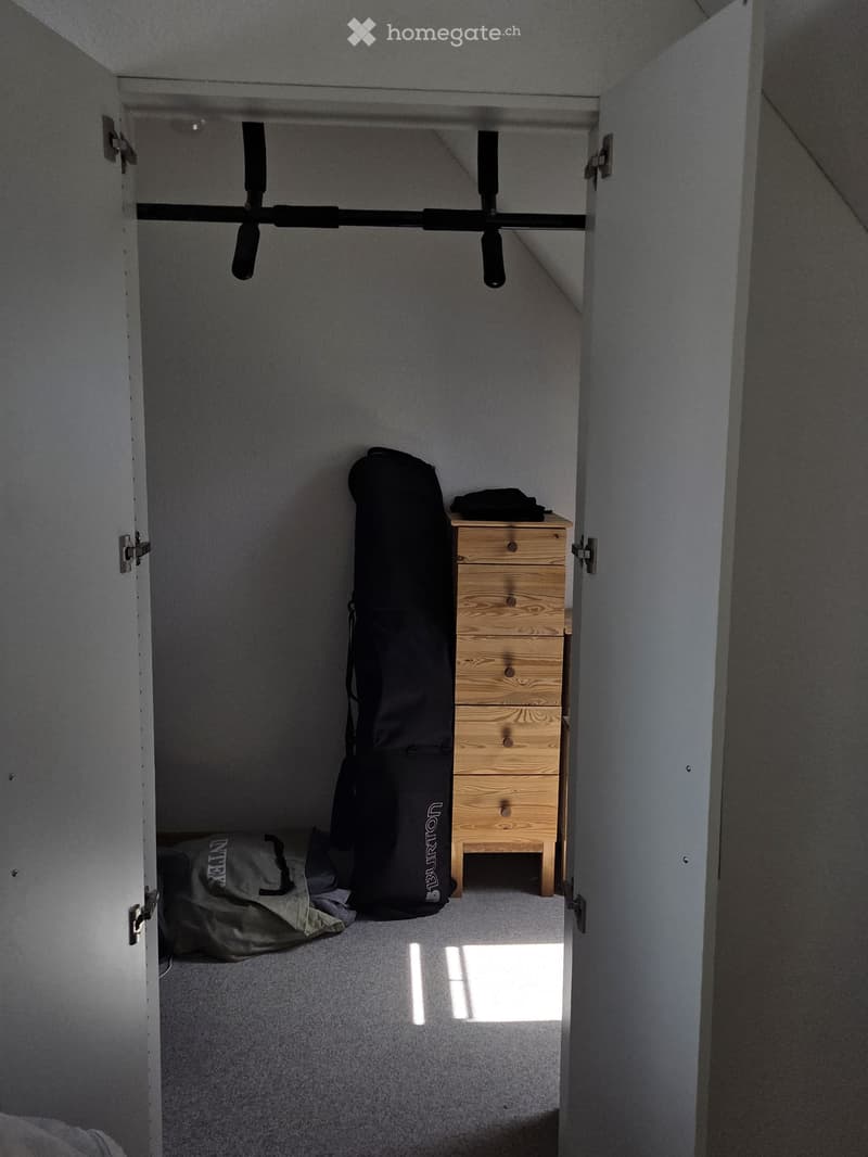 Small, narrow room with a wooden chest of drawers, a large black gym bag, and a backpack on the floor.
