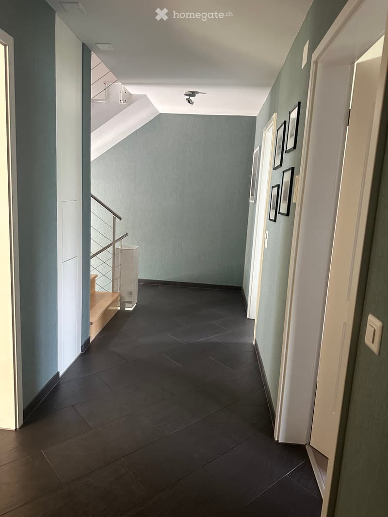 Modern hallway with dark tiled floor, light blue walls, white doors, and framed artwork. Features a staircase with a metal railing on the left side.