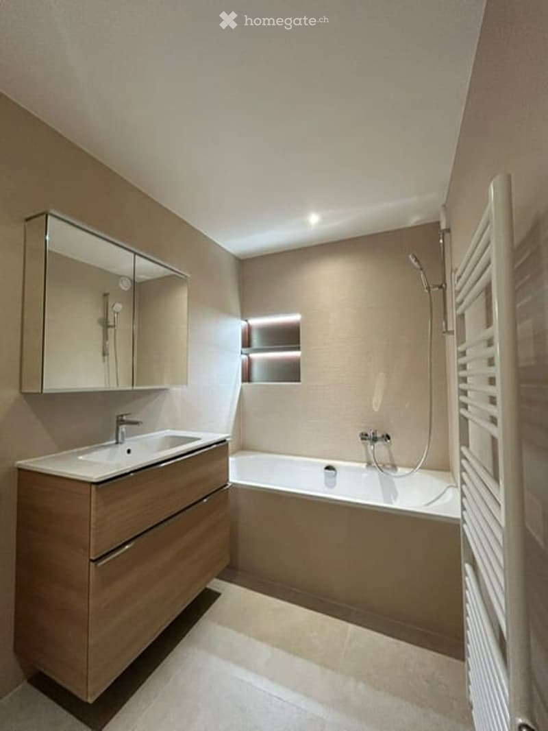 Modern bathroom with a wooden vanity, sink, mirror, bathtub, and showerhead. The space features warm lighting and a clean, contemporary design.