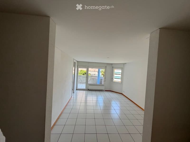 Empty hallway with white tiled flooring, white walls, and a large glass door leading to an outdoor area.