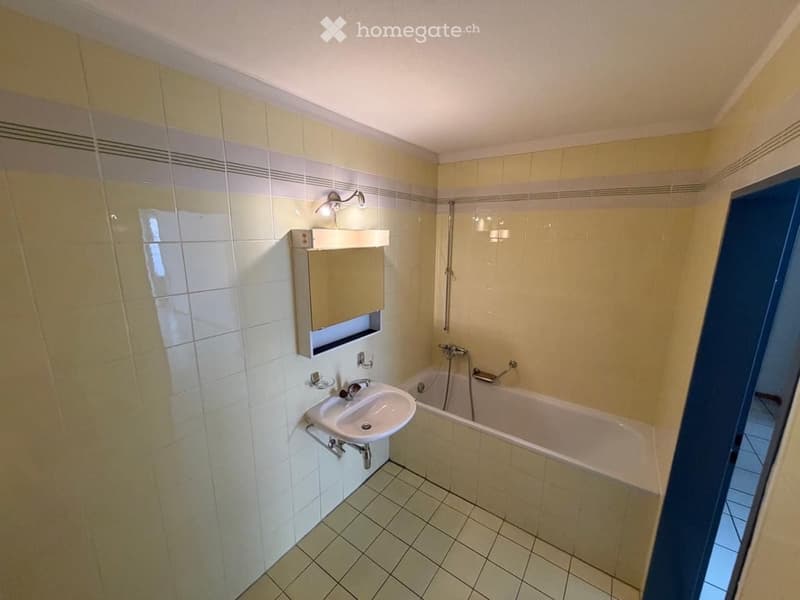 Bathroom with a white tiled sink, bathtub, mirror cabinet, and light fixture above the sink.