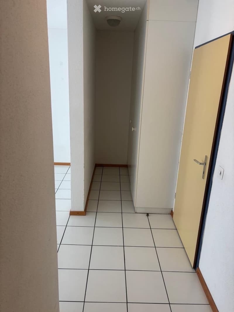 Empty hallway with white tiled flooring, white walls, and a closed door on the right side.