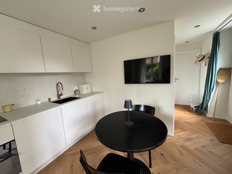Modern kitchen and dining area with white cabinets, a black dining table with chairs, a sink with a modern faucet, and a mounted TV screen.