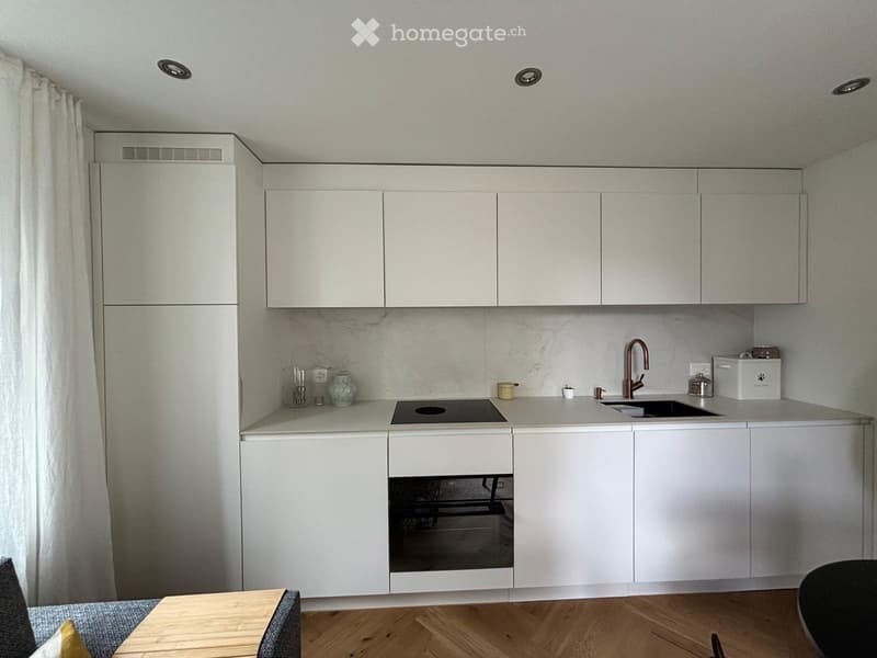 Modern kitchen with white cabinets, stainless steel appliances, marble backsplash, and a small dining area with a wooden table and chairs.