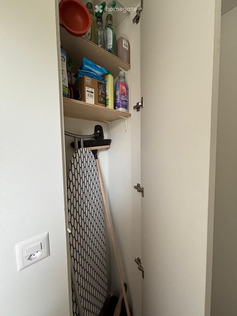 Open closet with shelves containing cleaning supplies, an ironing board, and a broom.