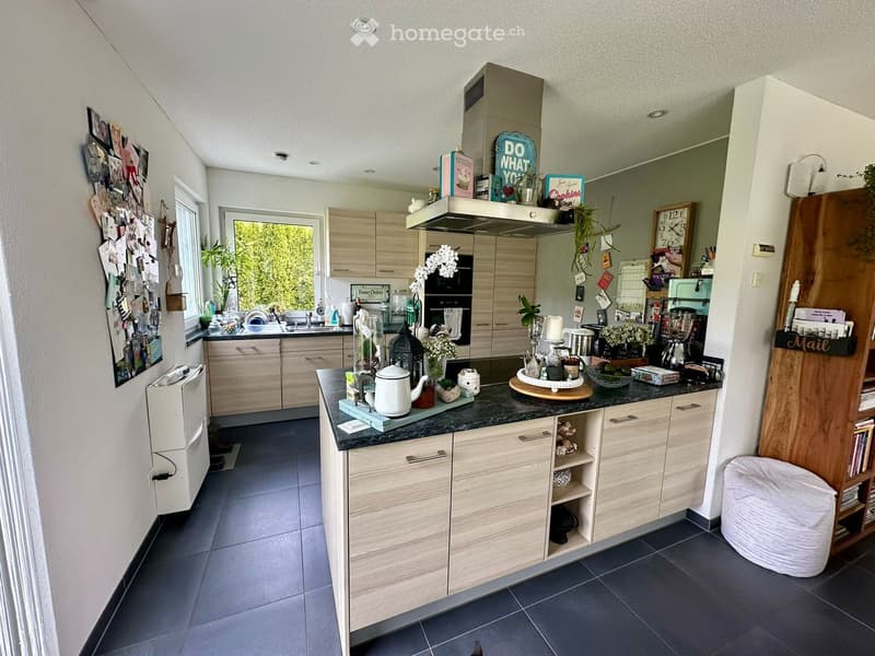 Modern kitchen with light wooden cabinets, dark granite countertop, and various appliances and decorative items.