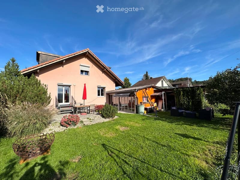 A well-maintained garden with a lawn, patio furniture, and a small seating area near the house.
