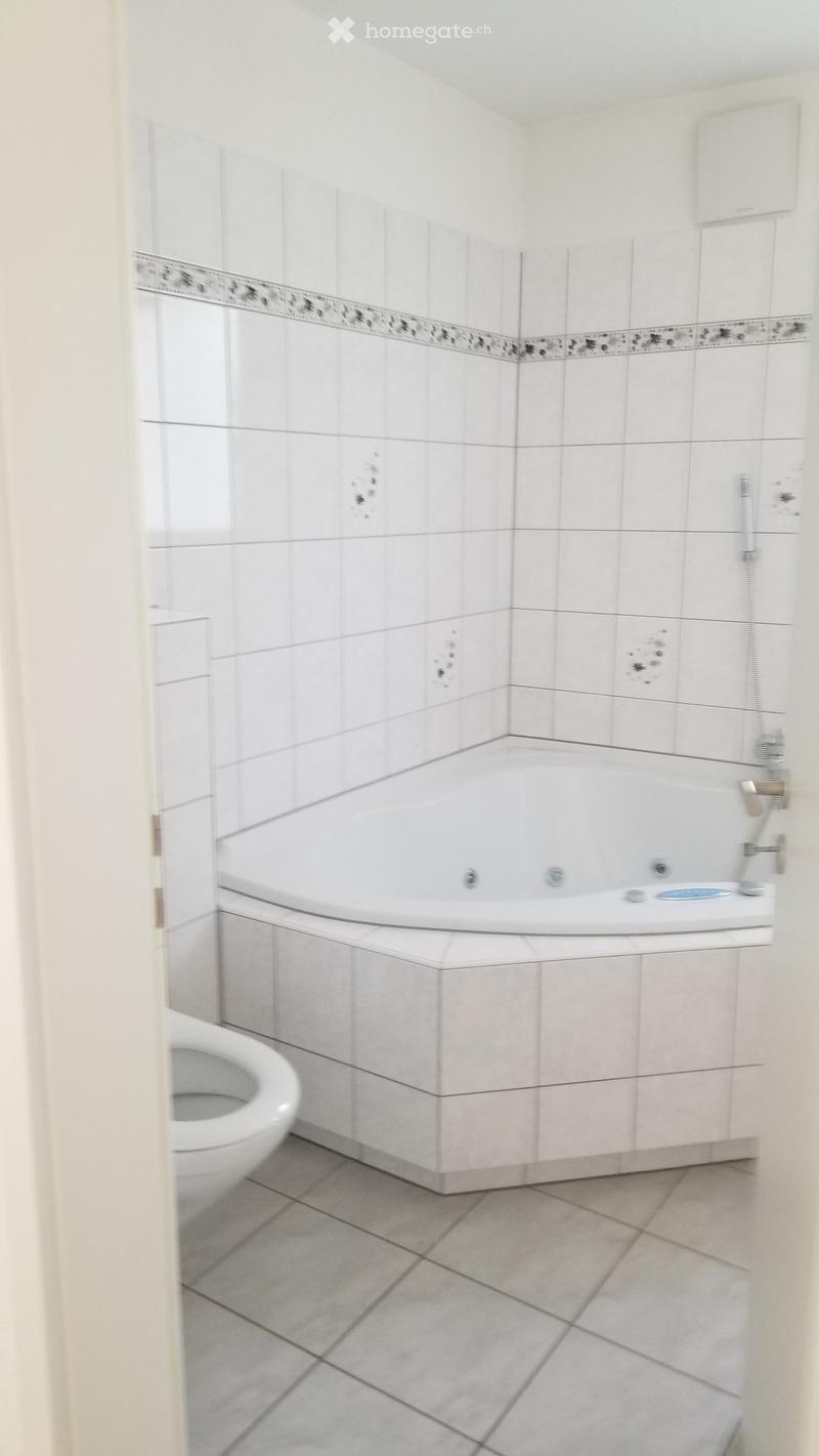 Bathroom with white tiled walls, a bathtub, a toilet, and a faucet.
