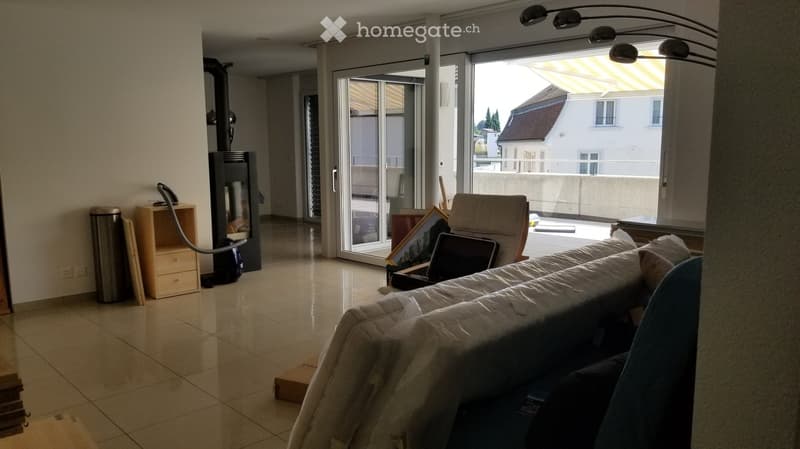 Living room with a sofa, chair, fireplace, and large sliding glass doors leading to a balcony. The room includes a small table, a cabinet, and a laptop on the floor.
