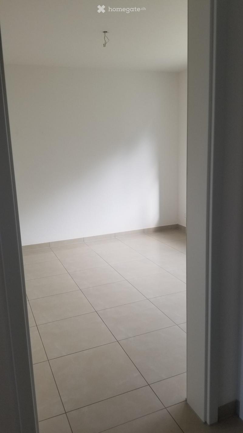 Empty room with beige tiled floor and white walls, viewed through an open doorway.