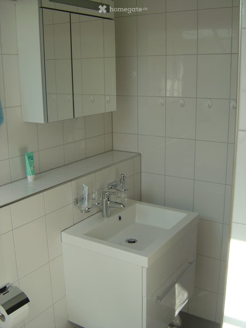 Modern bathroom with a white sink, chrome faucet, mirrored cabinet, and tiled walls.