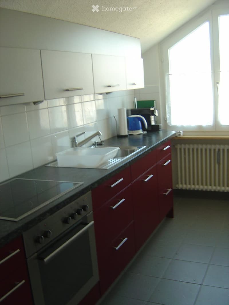 Modern kitchen with red cabinets, black countertop, stainless steel oven, sink, and various appliances including a coffee maker and electric kettle.
