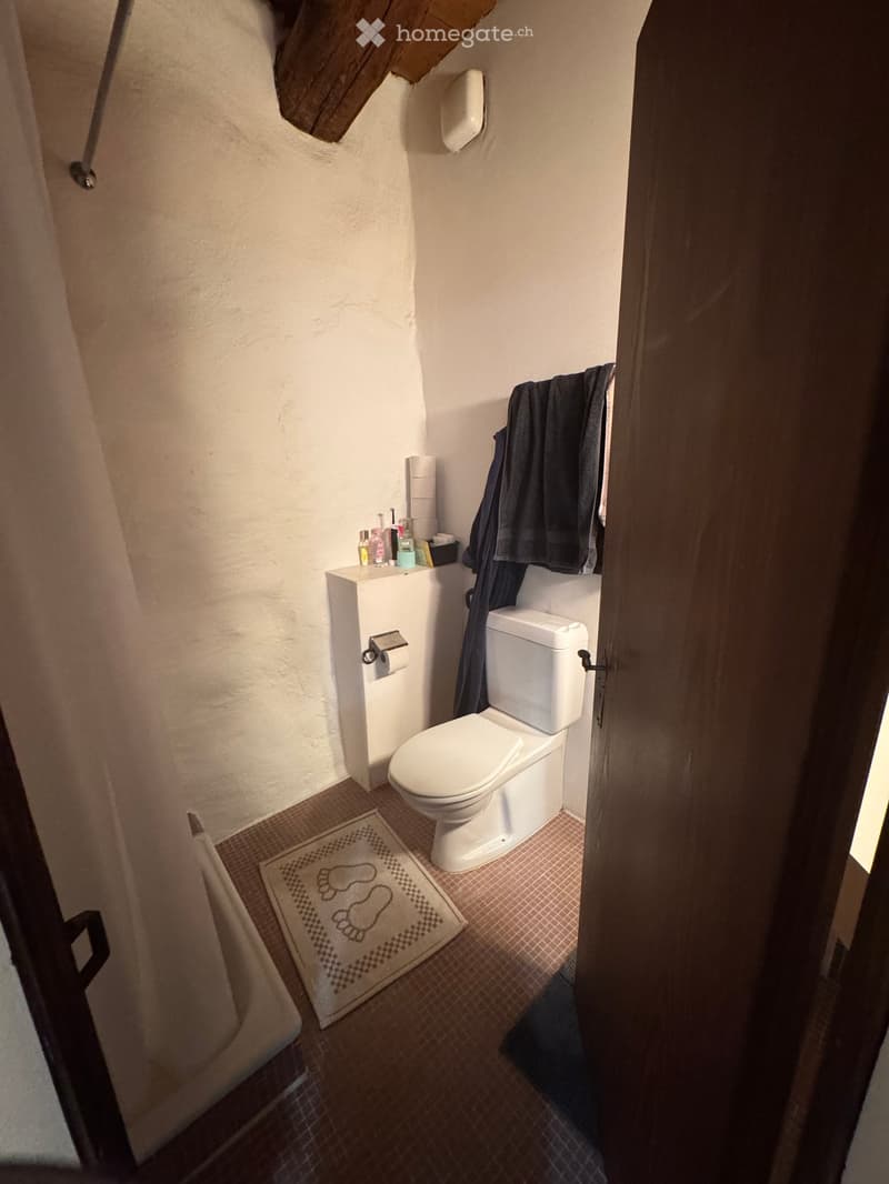 Small bathroom with a toilet, towel, toilet paper, and a rug with footprints on the floor.