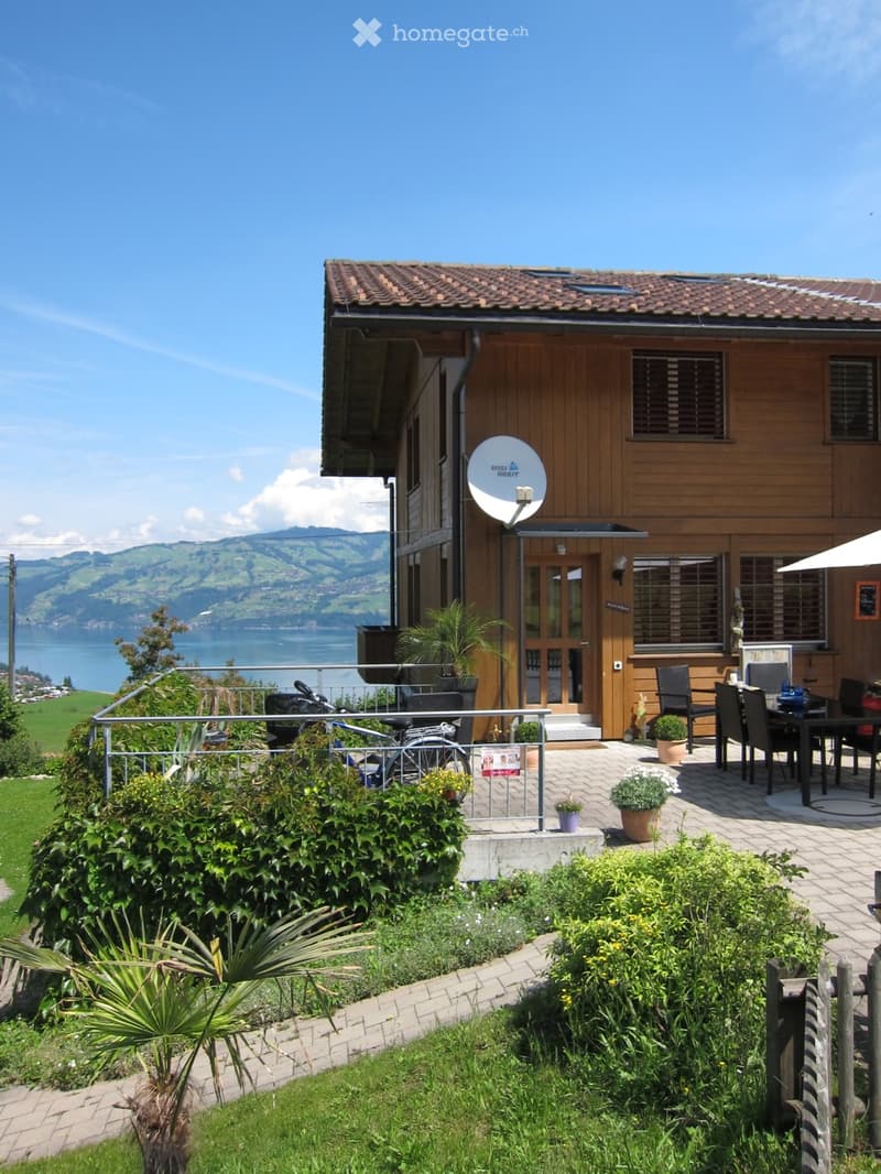 A well-maintained garden area with a patio, outdoor furniture, potted plants, and a scenic view of a lake and mountains.