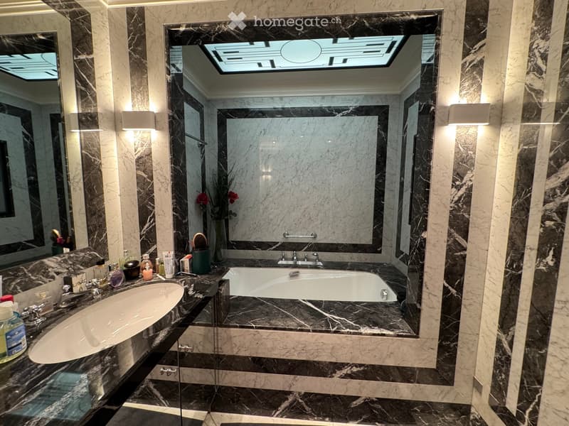 Luxurious bathroom with marble walls and floors, a large mirror, a bathtub, a sink, and decorative items on the counter.