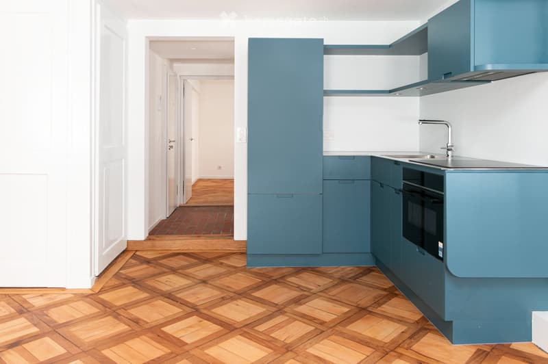 Modern kitchen with blue cabinets, wooden herringbone flooring, stainless steel sink, and built-in oven.