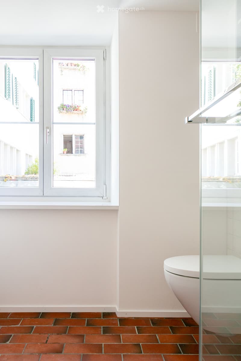 Bathroom with red brick floor, white walls, large windows, and a glass shower enclosure.