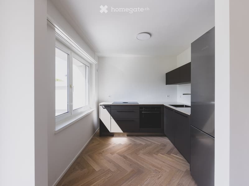 Modern kitchen with dark grey cabinets, stainless steel appliances, and wooden flooring.