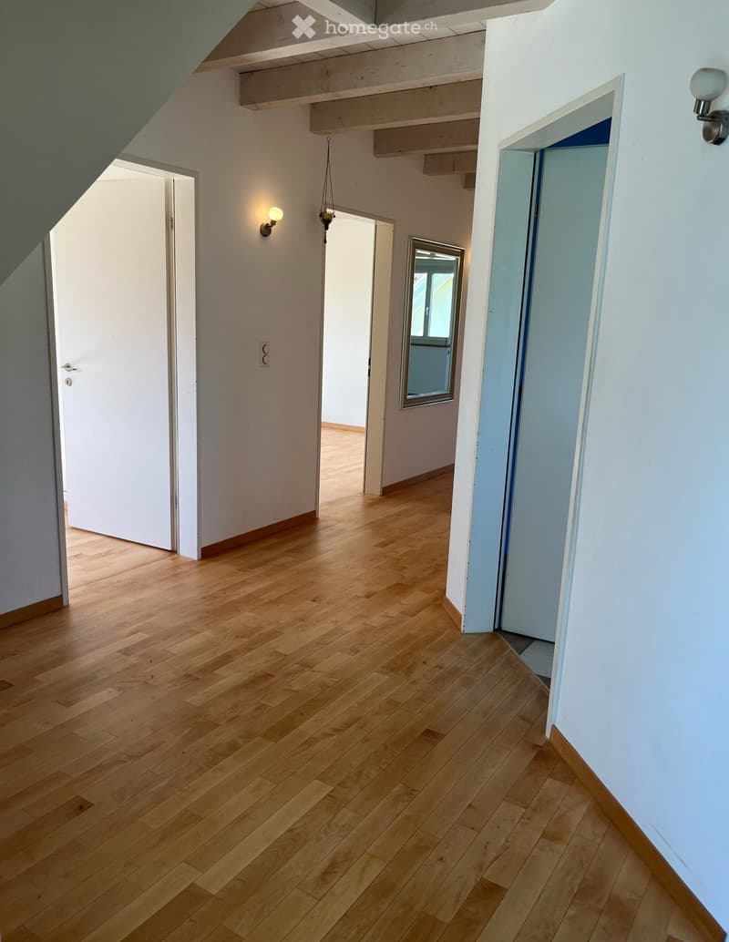 Empty hallway with wooden flooring, white walls, and several doors leading to other rooms.