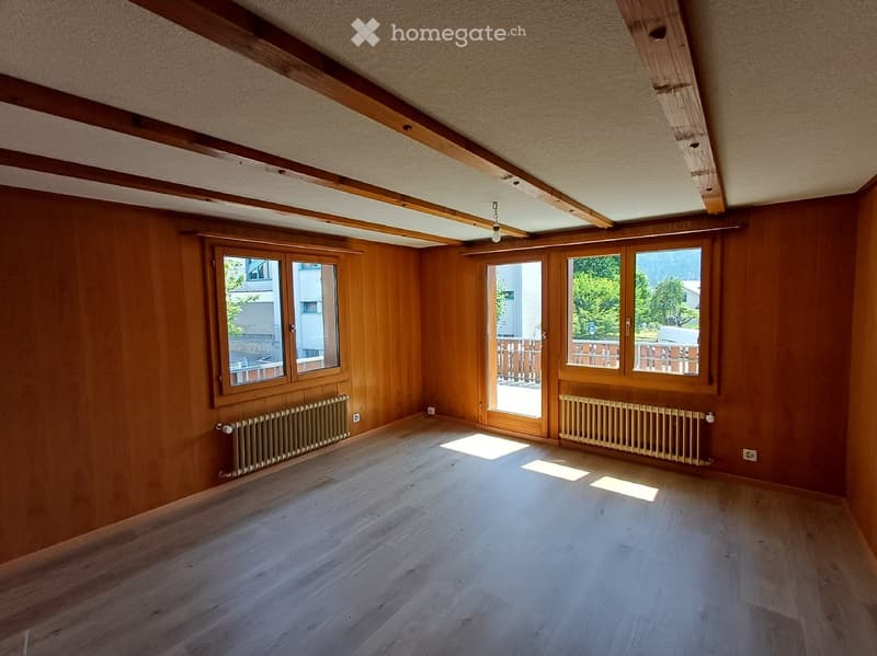 Empty room with wooden walls, wooden floor, large windows, radiators, and exposed wooden beams on the ceiling.