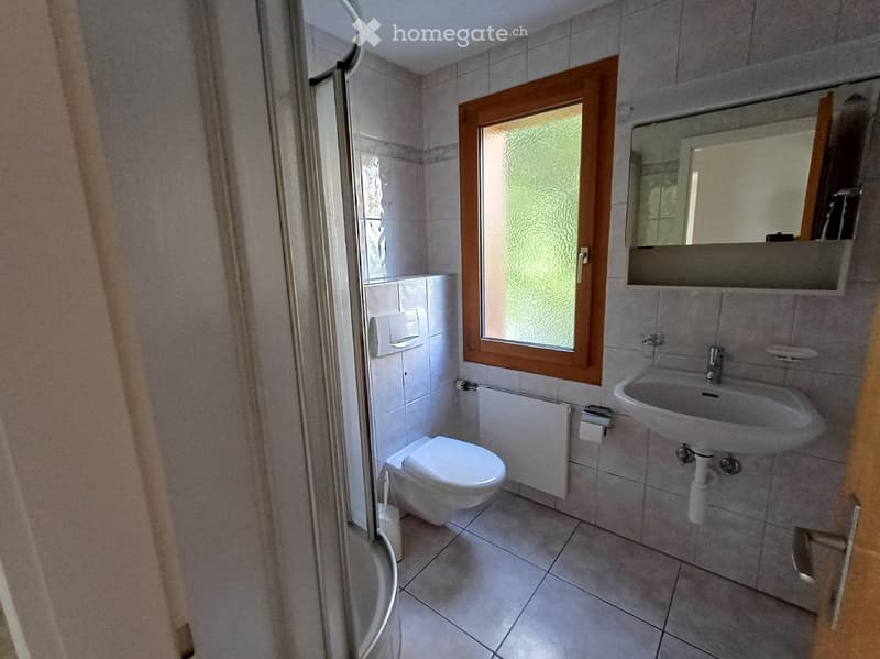 Modern bathroom with white tiles, a toilet, a sink with a mirror, and a shower area with a glass door.